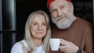 To eldre personer drikker kaffe og ser inn i kamera